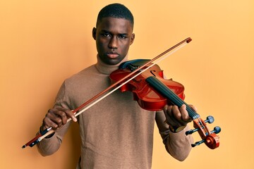 Young african american man playing violin skeptic and nervous, frowning upset because of problem....