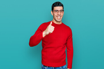 Handsome hispanic man wearing casual clothes and glasses doing happy thumbs up gesture with hand....