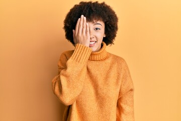 Fototapeta na wymiar Young hispanic girl wearing wool winter sweater covering one eye with hand, confident smile on face and surprise emotion.