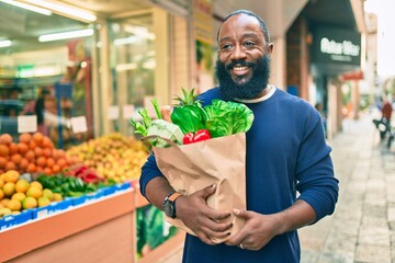 African american man with beard holding paper bag of groceries from supermarket