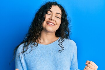 Fototapeta premium Young brunette woman with curly hair wearing casual clothes very happy and excited doing winner gesture with arms raised, smiling and screaming for success. celebration concept.