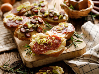 Bruschetta with cheese, salami, sausage and herbs served on a board, close up view
