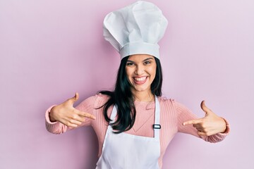 Young hispanic woman wearing baker uniform and cook hat looking confident with smile on face,...