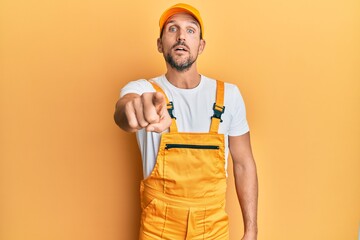 Young handsome man wearing handyman uniform over yellow background pointing displeased and frustrated to the camera, angry and furious with you