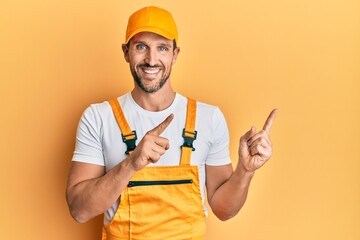 Young handsome man wearing handyman uniform pointing to the side smiling with a happy and cool smile on face. showing teeth.