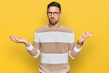 Handsome man with beard wearing casual clothes and glasses clueless and confused with open arms, no...