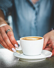 Closeup female barista hands holding cup of aromatic latte or cappuccino coffee in bar or cafe