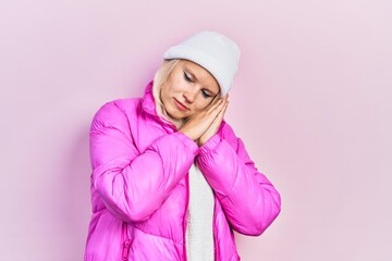Beautiful caucasian blonde woman wearing wool hat and winter coat sleeping tired dreaming and...