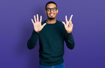 Fototapeta premium Young african american man wearing casual clothes and glasses showing and pointing up with fingers number eight while smiling confident and happy.