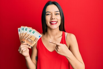 Young hispanic girl holding euro banknotes smiling happy pointing with hand and finger