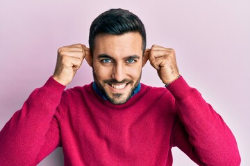 Young hispanic man wearing casual clothes smiling pulling ears with fingers, funny gesture....