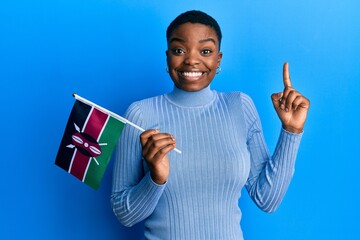 Young african american woman holding kenya flag smiling with an idea or question pointing finger...
