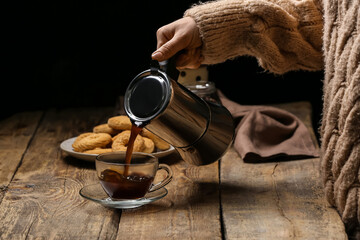 Naklejka premium Woman pouring hot coffee into cup on wooden table