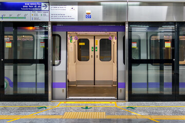 View of a metro train with open doors standing at the platform for passengers during the rush hour at a metro station in East West Metro system Kolkata, West Bengal, India - obrazy, fototapety, plakaty