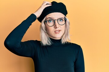 Young blonde girl wearing french look with beret confuse and wonder about question. uncertain with doubt, thinking with hand on head. pensive concept.