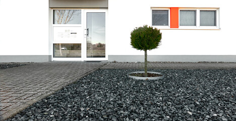 Front yard at new apartment building with gray gravel stones and a lone small tree