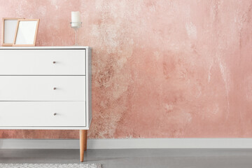 Stylish chest of drawers with frames and candle near color wall