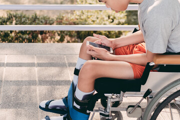 Obraz premium Asian special child on wheelchair using a smartphone on the ramp for disabled people background, Social of communication, Life in the education age of disabled children, Happy disability kid concept.