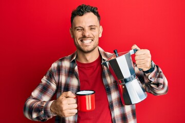 Young hispanic man drinking italian coffee winking looking at the camera with sexy expression,...