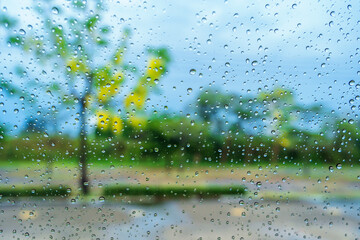 Rain droplets on surface of car glass with blurred green nature background and flowers through window glass of car. Freshness after rain. Soft focus, Selective focus on waterdrops. Natural background