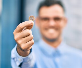 Young hispanic businessman smiling happy holding 1 euro coin at the city.