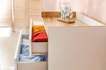 Stylish chest of drawers with clothes in room, closeup