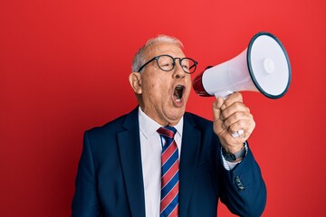 Senior grey-haired businessman screaming using megaphone over isolated red background.