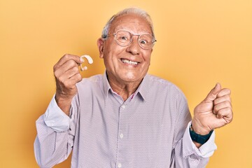Senior man with grey hair holding medical hearing aid screaming proud, celebrating victory and...