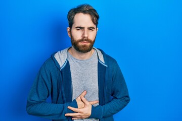 Caucasian man with beard wearing casual sweatshirt with hand on stomach because indigestion, painful illness feeling unwell. ache concept.