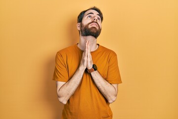 Caucasian man with beard wearing casual yellow t shirt begging and praying with hands together with hope expression on face very emotional and worried. begging.