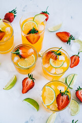 Fresh orange strawberry mojito in different glasses with ice cubes and slices of lime on the table. Summer refreshing drink