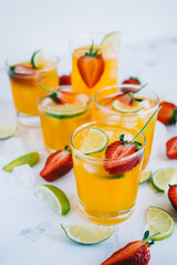 Fresh orange strawberry mojito in different glasses with ice cubes and slices of lime on the table. Summer refreshing drink