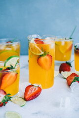 Fresh orange strawberry mojito in different glasses with ice cubes and slices of lime on the table. Summer refreshing drink