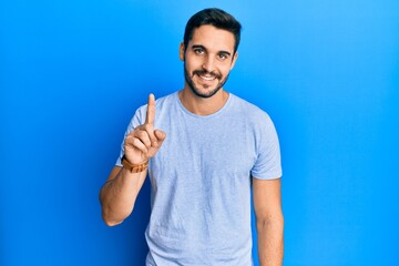 Young hispanic man wearing casual clothes smiling with an idea or question pointing finger up with happy face, number one