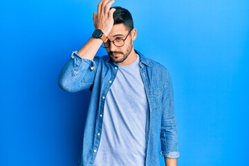 Young hispanic man wearing casual clothes and glasses surprised with hand on head for mistake,...