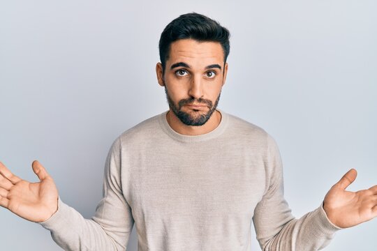 Young hispanic man wearing casual clothes clueless and confused with open arms, no idea and doubtful face.