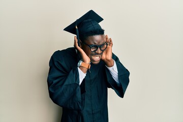 Handsome black man wearing graduation cap and ceremony robe trying to hear both hands on ear gesture, curious for gossip. hearing problem, deaf