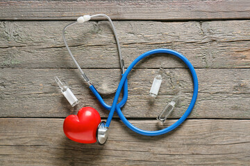 Modern stethoscope with heart and ampules on wooden background