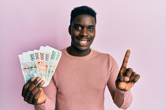 Handsome black man holding czech koruna banknotes smiling with an idea or question pointing finger with happy face, number one