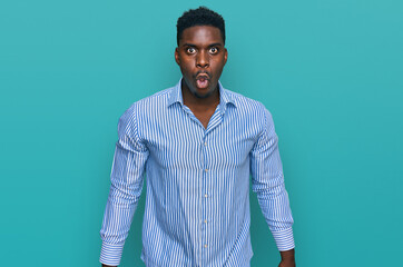Obraz premium Handsome business black man wearing casual striped t shirt scared and amazed with open mouth for surprise, disbelief face