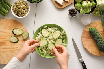 Woman cooking tasty salad with fresh vegetables on light background