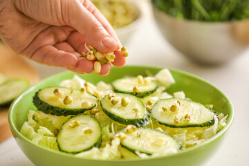 Woman cooking tasty salad with fresh vegetables on light background