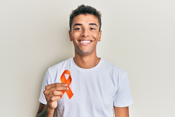 Young handsome african american man holding awareness orange ribbon looking positive and happy...