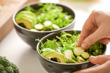 Woman making tasty salad with fresh vegetables on light table