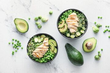 Bowls of tasty salad with fresh vegetables and chicken on light background