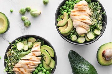 Bowls of tasty salad with fresh vegetables and chicken on light background
