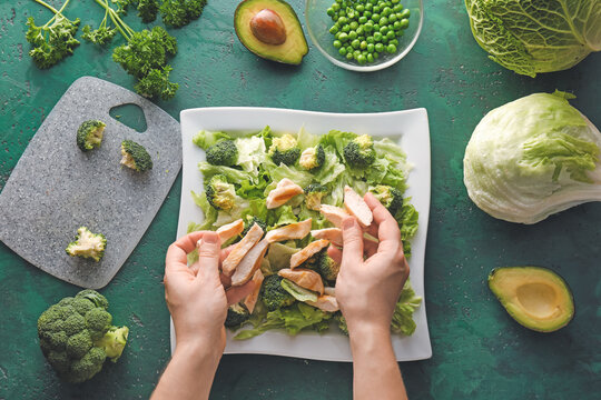 Woman making tasty salad with fresh vegetables and chicken on color background