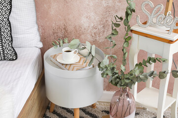 Bedside table with cup of coffee and book near color wall in room