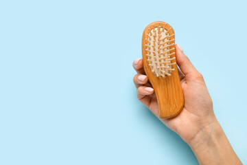 Female hand with wooden hair brush on color background