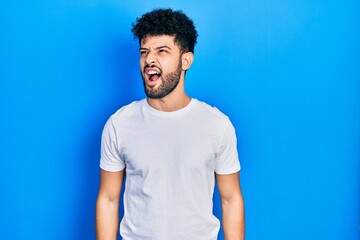 Obraz premium Young arab man with beard wearing casual white t shirt angry and mad screaming frustrated and furious, shouting with anger. rage and aggressive concept.